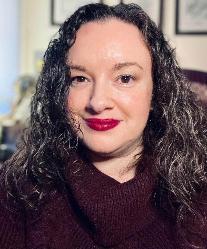 A white woman with brown, curly hair and red lipstick.